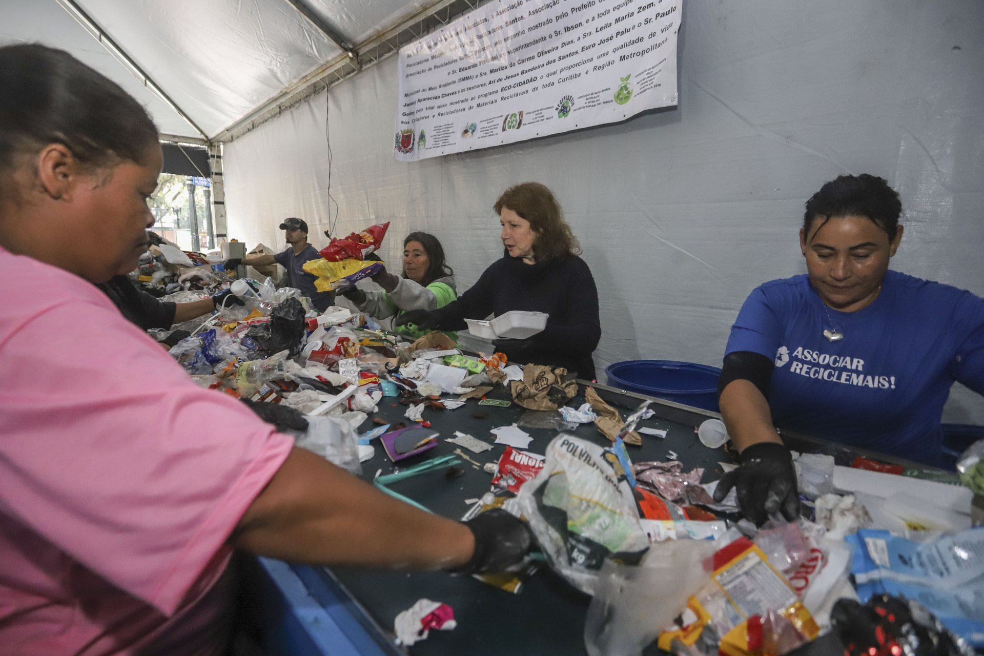 Mãos separando materiais recicláveis por tipo na mesa de triagem
